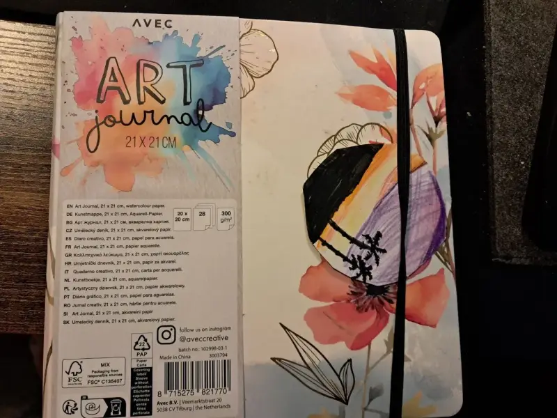 Pierwsza strona szkicownika z napisem "ART journal" i kolorowymi kwiatami. Na okładce widoczny fragment rysunku.